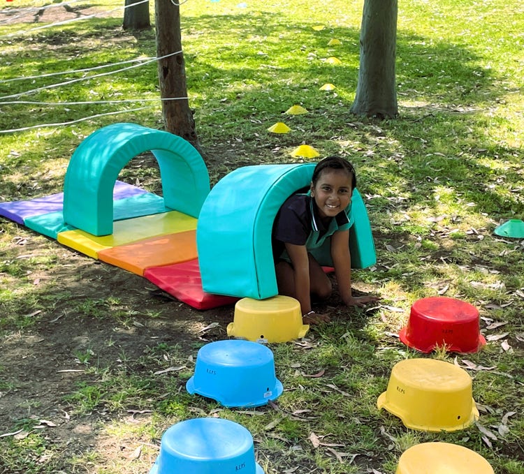 a girl playing wth colourful and soft sport equipment. She is climbing through a small tunnel.