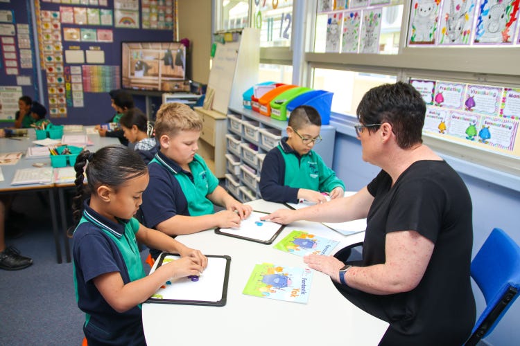 a teacher working with three students with whiteboards and books