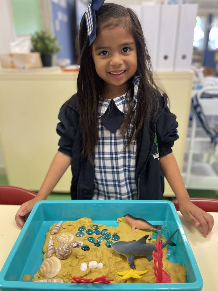 a girls lookign at the camera and showing her work which is playdough and animals