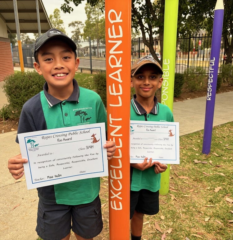 2 boys standing next to colourful poles, holding certificates