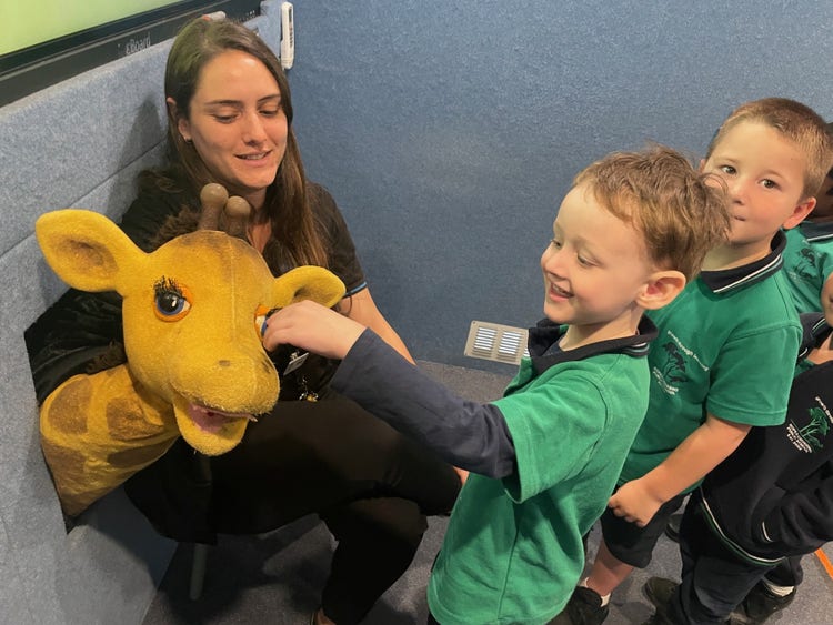 2 students and and an adult with a puppet giraffe