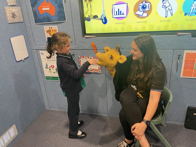 a lady holding a giraffe puppet and a girl patting the puppet