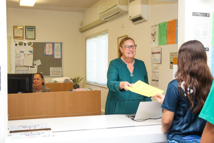 a lady stading in an office passing a sheet to a student